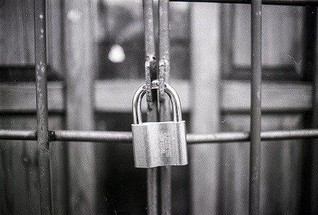 A black and white photo of a padlock on a fence.